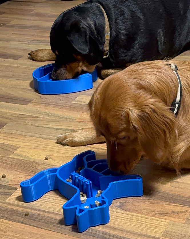 Two dogs eating kibbles from a blue slow feeder bowls on a wooden floor.