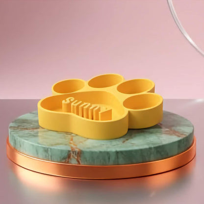 Yellow paw-shaped slow feeder bowl on a green marble stand with a pink background