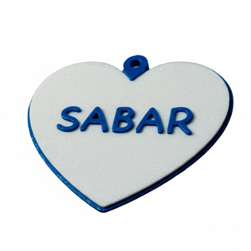 Heart-shaped white pendant with blue border and 'SABAR' text on a light gray background