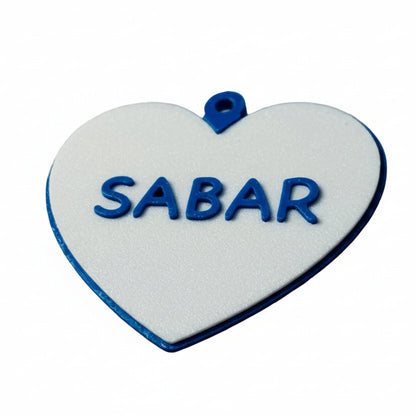 Heart-shaped white pendant with blue border and 'SABAR' text on a light gray background