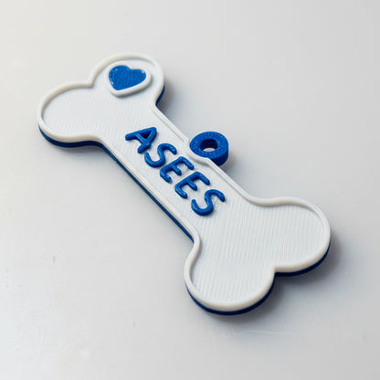 Bone-shaped dog name tag with 'ASEES' text on a gray background