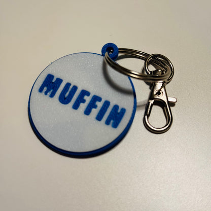 Keychain with a round dog name tag labeled 'MUFFIN' on a plain background