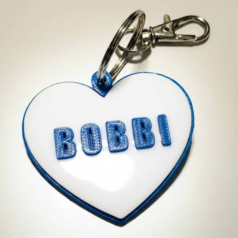 Heart-shaped keychain dog name tag with 'BOBBI' on a light gray background