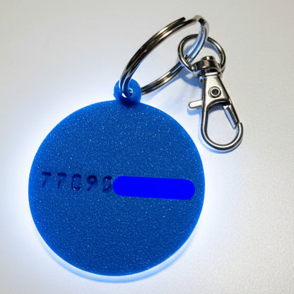 Blue round keychain dog name tag with embossed text on a light gray background