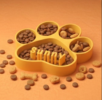 Yellow paw-shaped pet feeder filled with dog food on an orange background