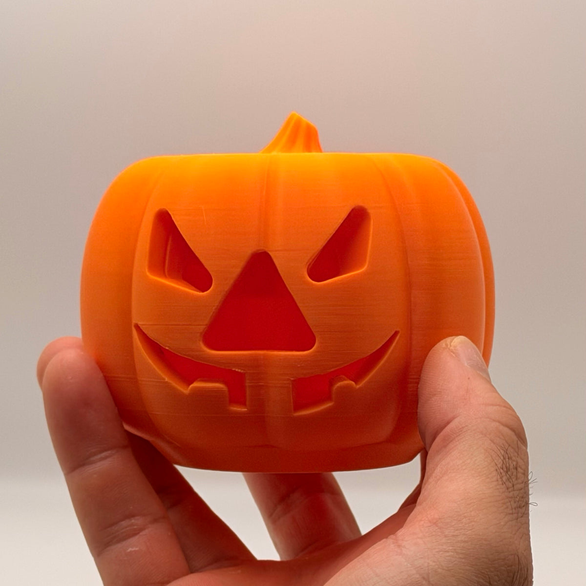 Orange pumpkin treat dispenser for dogs and cats, held in a hand to show size