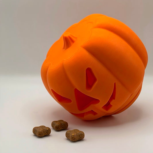 Orange pumpkin treat dispenser for dogs and cats, with kibble beside it